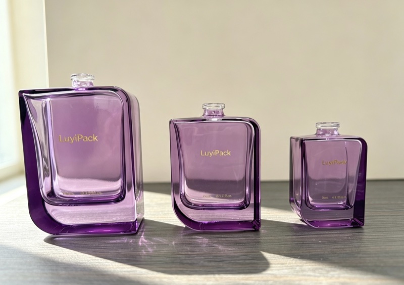 Three violet glass shoulder bottles without caps on a table